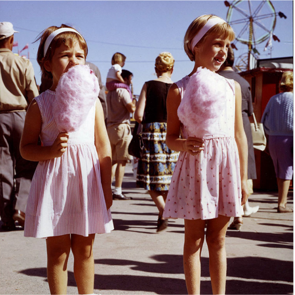 Coloured image of two girls eating cotton candy in the midway.